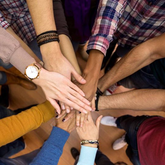 Hands of Teens and Adults reaching for the center of the image